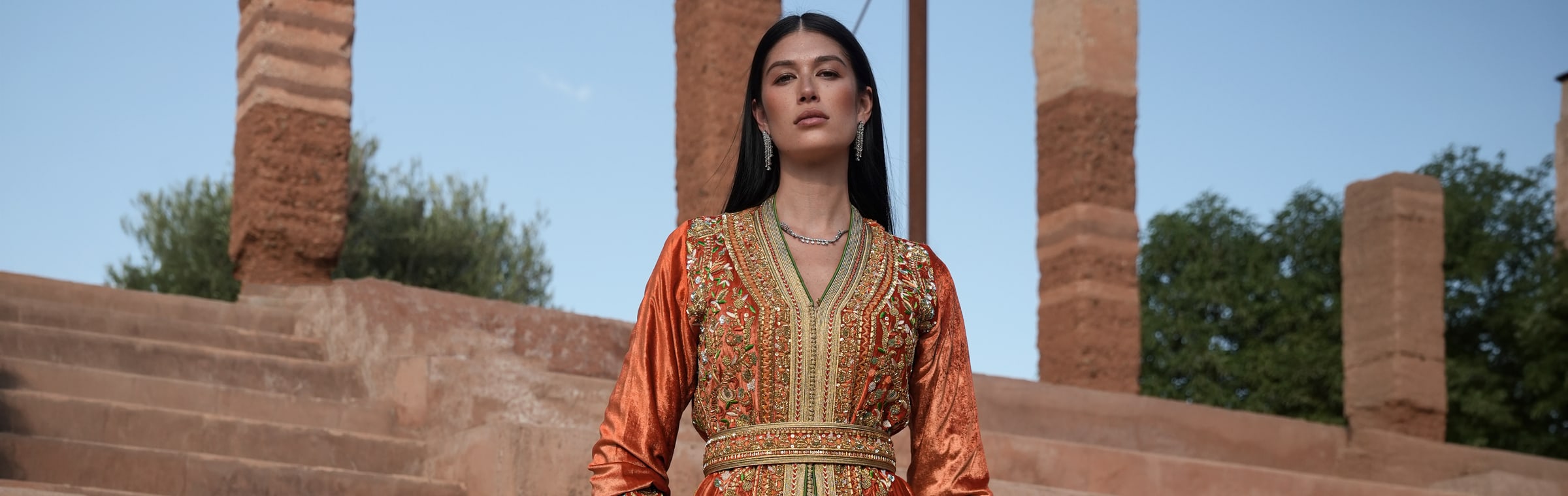 Summer Fall 2026 collection by Bouchra Filali Lahlou, a rust velvet Moroccan kaftan on the steps of a Marrakech riad