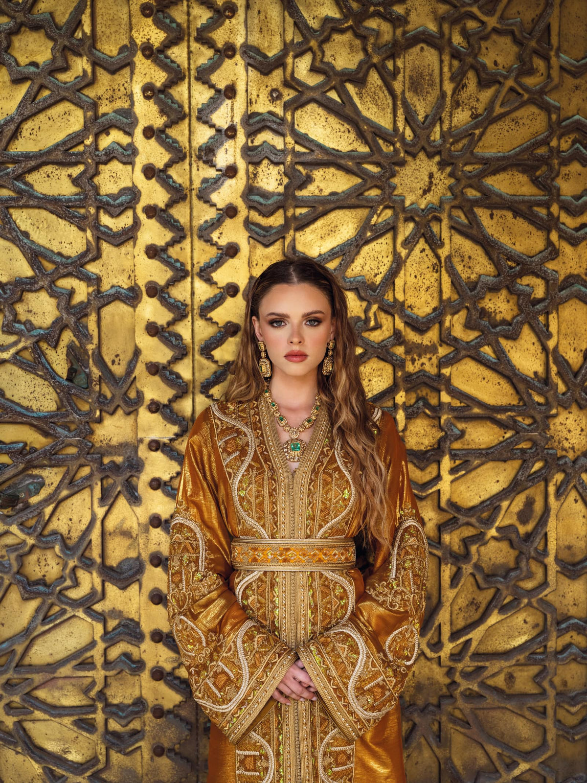 Un caftan marocain bronze aux broderies dorées, photographié devant une porte en laiton sculpté.
