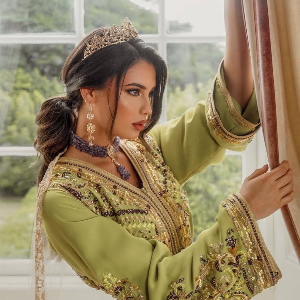 Un caftan marocain vert aux broderies travaillées sur l’encolure et les poignets, porté près d’une fenêtre.